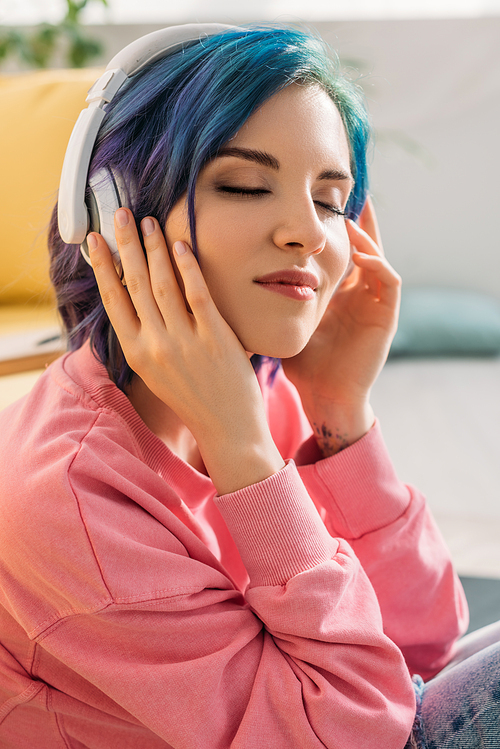 Beautiful woman with colorful hair and closed eyes in headphones listening music and smiling