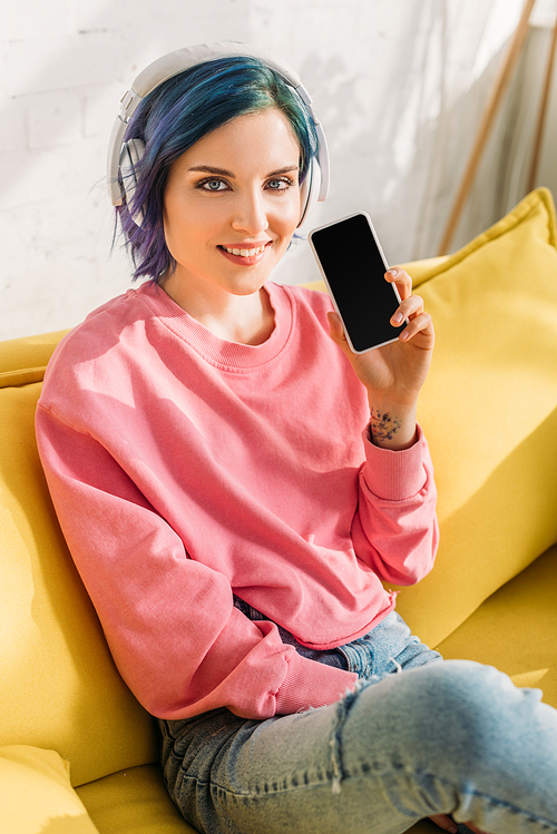 High angle view of woman with colorful hair and headphones smiling,  and showing smartphone