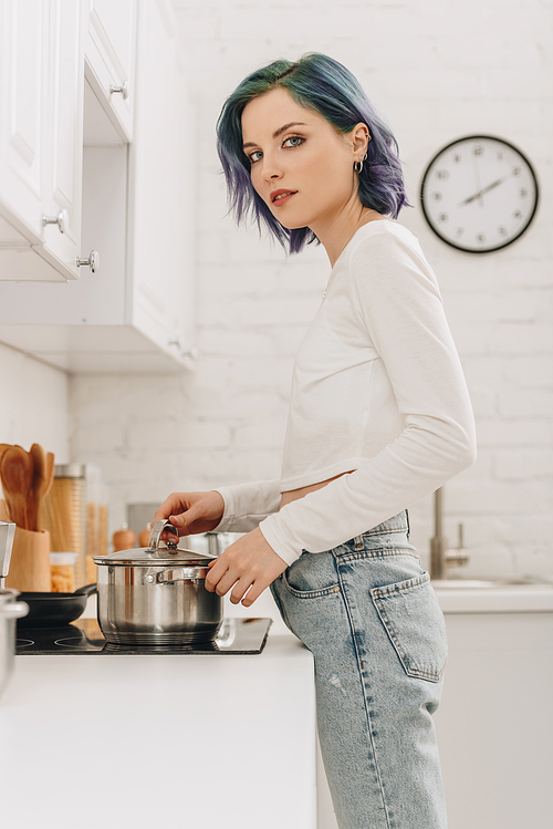 Low angle view of of girl with colorful hair touching pan lid near kitchen stove and 