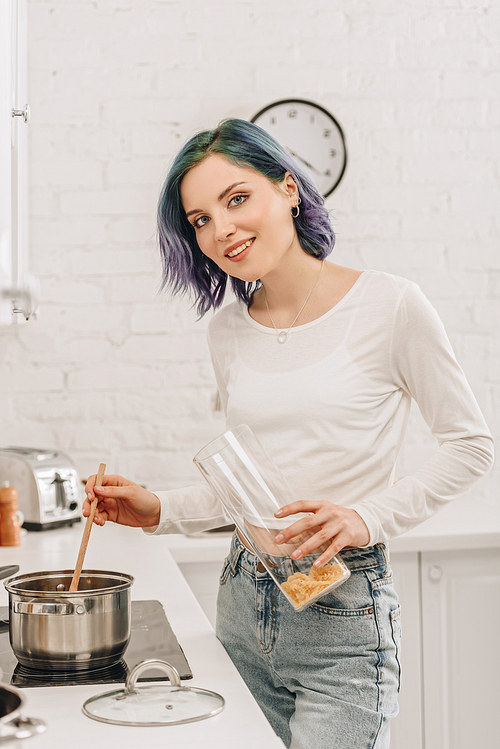 Selective focus of girl with colorful hair smiling,  and preparing soup in kitchen