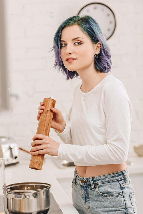 Selective focus of girl with colorful hair smiling and  with pepper mill above pan in kitchen