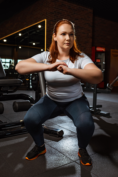 focused overweight girl squatting with clenched hands in gym