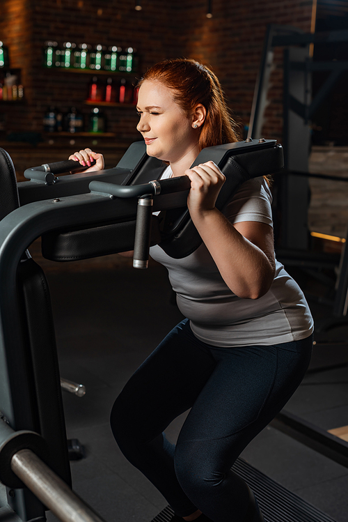 concentrated overweight girl doing arms extension exercise on fitness machine