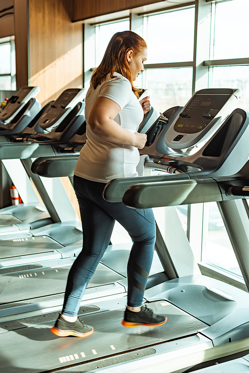overweight girl working out on treadmill in gym near window