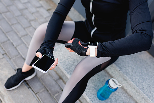 cropped view of young sportswoman with fitness tracker on hand holding smartphone with blank screen