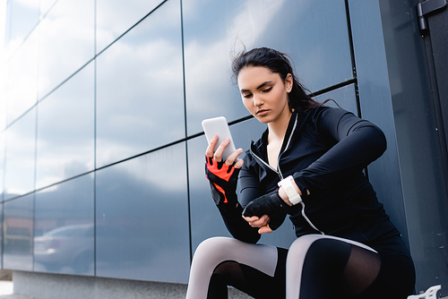 young sportswoman holding smartphone and looking at fitness tracker