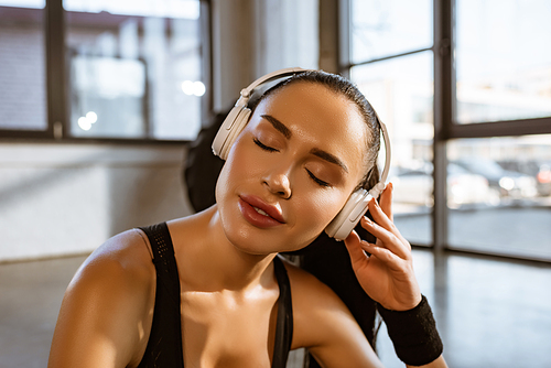 Portrait of sportswoman with closed eyes listening music in headphones in gym
