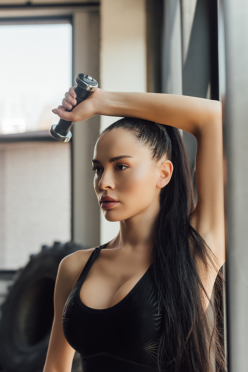 Beautiful sportswoman holding dumbbell over head in gym
