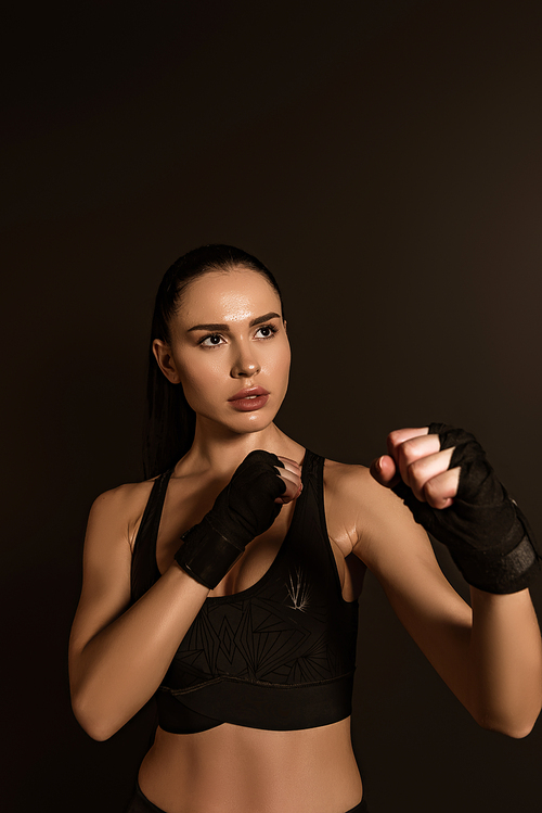 Sportswoman in sports gloves standing in fighting position isolated on black