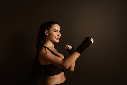 Sportswoman smiling and standing in fighting position isolated on black