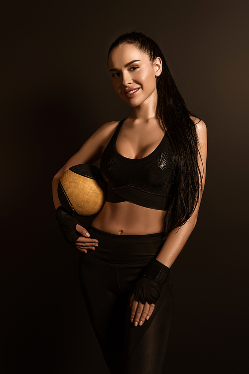 Brunette sportswoman with ball  and smiling isolated on black