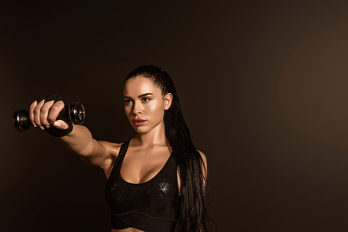 Brunette sportswoman holding dumbbell with outstretched hand isolated on black