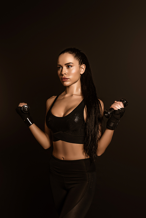 Beautiful sportswoman training with dumbbells isolated on black
