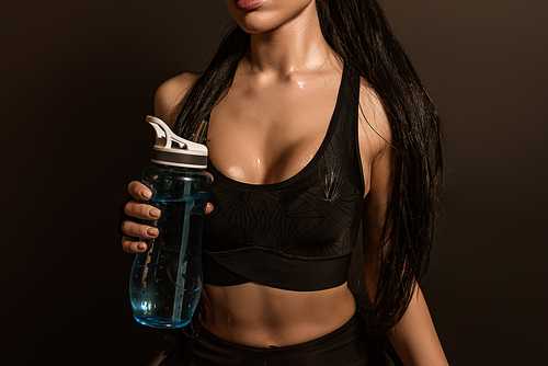 Cropped view of sexy sportswoman with sports bottle isolated on black