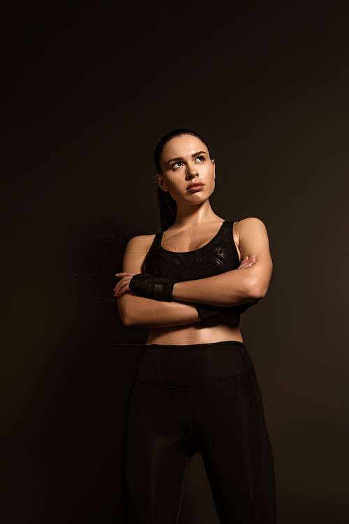 Front view of sportswoman with crossed arms looking away isolated on black