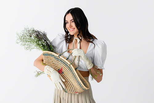 happy young woman in spring outfit holding straw bag with flowers isolated on white