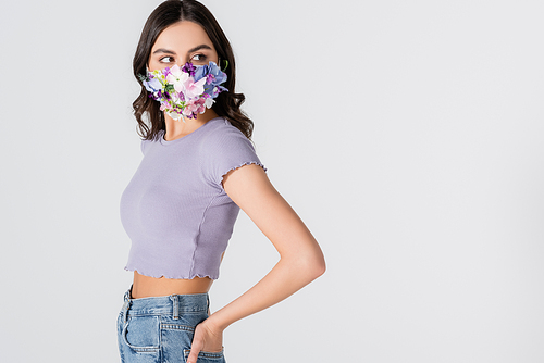 young woman in crop top and medical mask with blooming flowers looking away isolated on white