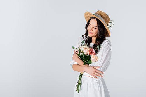 smiling woman in straw hat and dress holding bouquet of spring flowers isolated on white