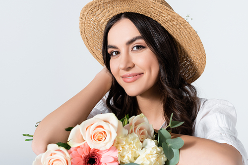 smiling young woman in straw hat holding bouquet of spring flowers isolated on white
