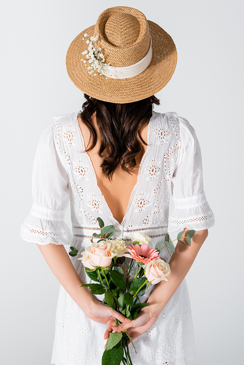 back view of woman in straw hat and dress holding bouquet isolated on white