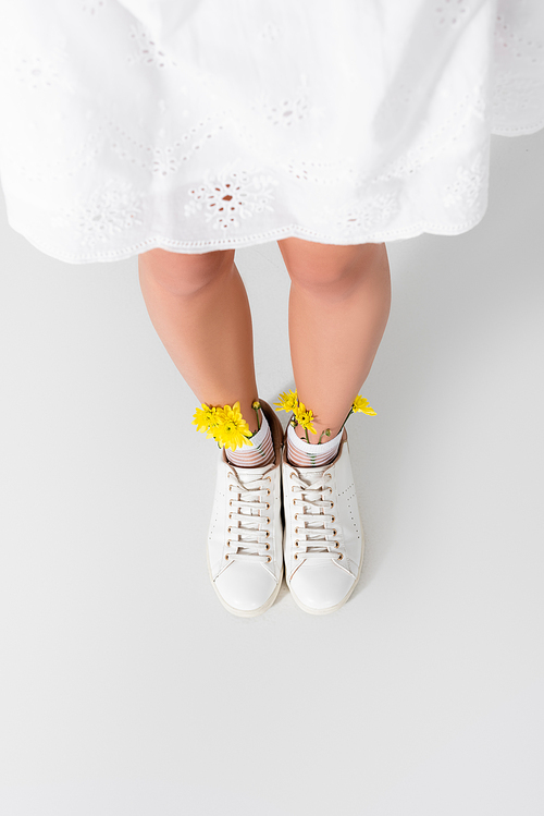 high angle view of model in sneakers with yellow spring wildflowers posing on white