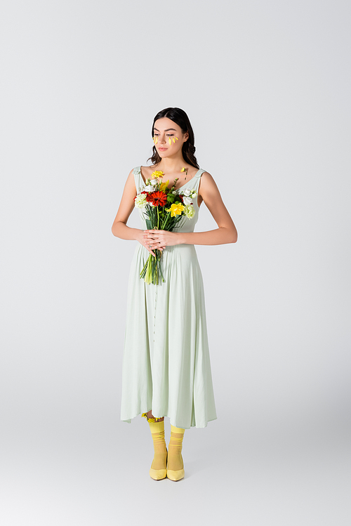 full length of young woman with petals on face holding bouquet of flowers isolated on white