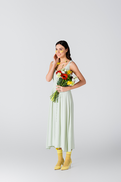 full length of young woman with petals on face holding bouquet of spring flowers on white