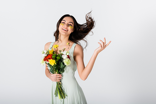 cheerful young woman with petals on face holding bouquet of flowers isolated on white
