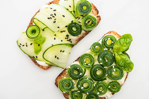 top view of fresh cucumber toasts with seeds and basil leaves isolated on white