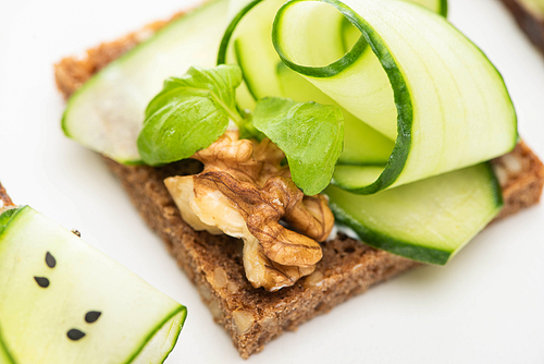 close up view of fresh cucumber toast with walnut and basil leaves isolated on white