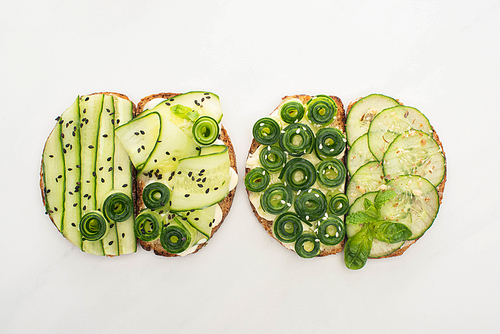 top view of fresh cucumber toasts with seeds, mint and basil leaves on white background