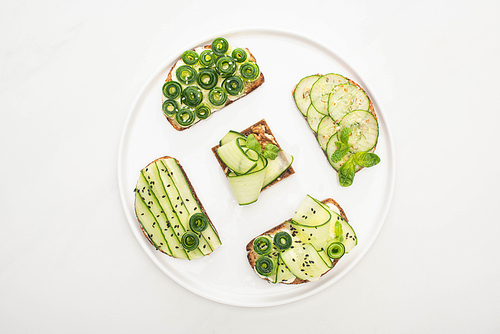 top view of fresh cucumber toasts with seeds, mint and basil leaves on round plate on white background