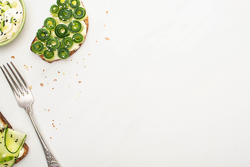 top view of fresh cucumber toasts with seeds near yogurt in bowl and fork on white background