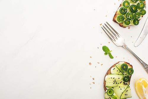 top view of fresh cucumber toasts with seeds, basil leaves and cutlery on white background