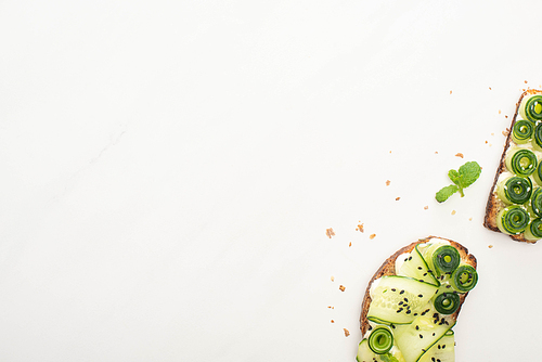 top view of fresh cucumber toasts with seeds, mint on white background