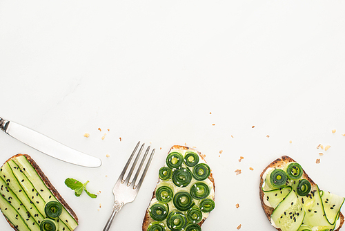 top view of fresh cucumber toasts with seeds, mint leaves and cutlery on white background