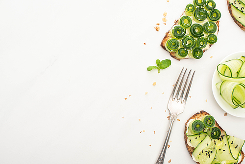 top view of fresh cucumber toasts with seeds, mint leaves and fork on white background