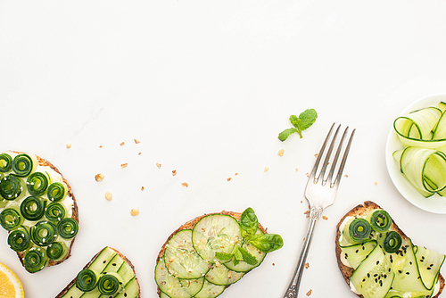top view of fresh cucumber toasts with seeds, mint and basil leaves and fork on white background