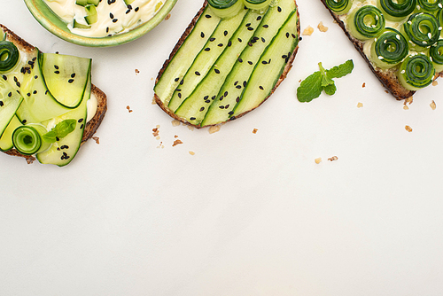 top view of fresh cucumber toasts with seeds, mint leaves near yogurt on white background