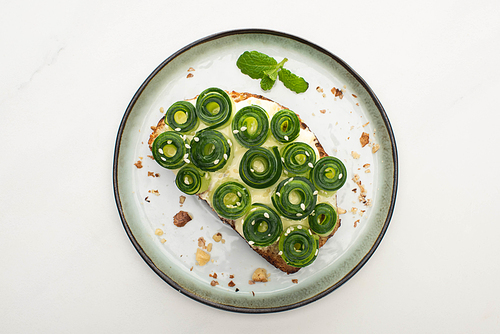 top view of fresh cucumber toast with sesame and mint leaves on plate on white background