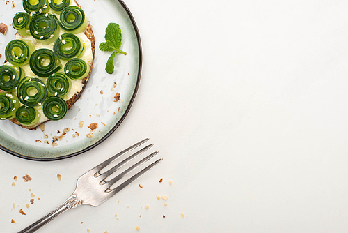 top view of fresh cucumber toast with sesame and mint leaves on plate near fork on white background