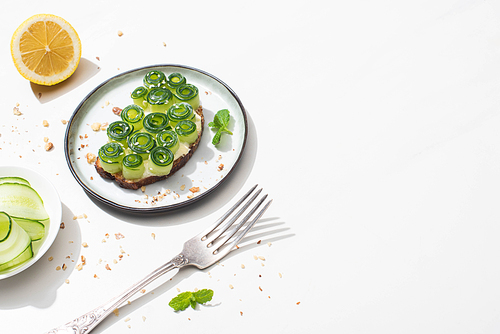 fresh cucumber toast with sesame and mint leaves on plate near fork and lemon on white background