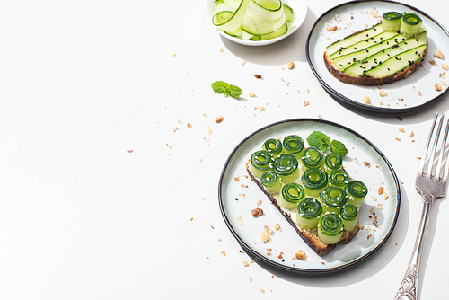 fresh cucumber toasts on plates near fork on white background