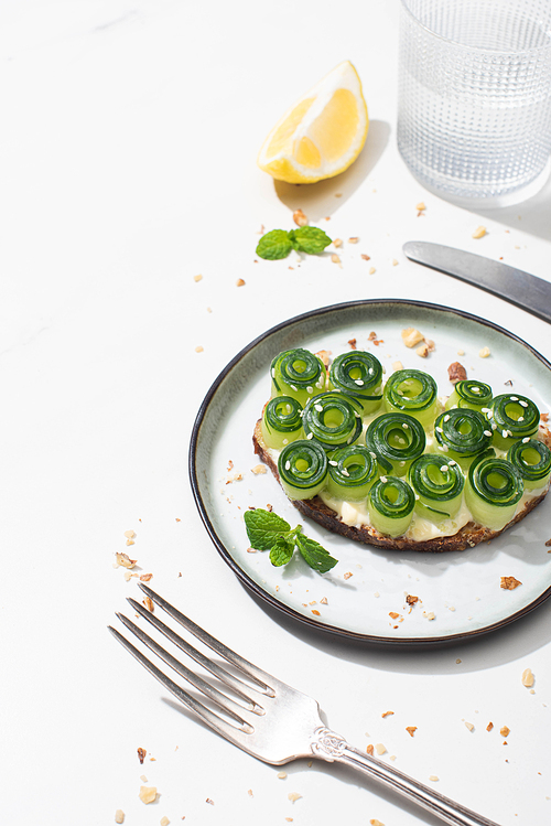 fresh cucumber toast with seeds served with cutlery, lemon and water on white background