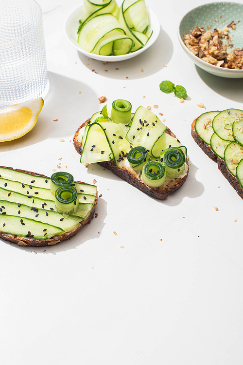 fresh cucumber toasts with seeds, mint leaves and lemon near glass of water on white background