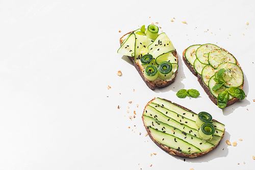 fresh cucumber toasts with seeds, mint and basil leaves on white background