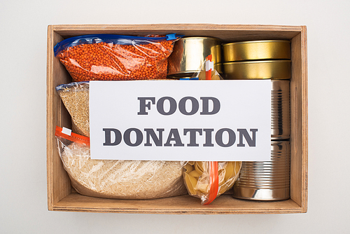 top view of cans and groats in zipper bags in wooden box with food donation card on white background