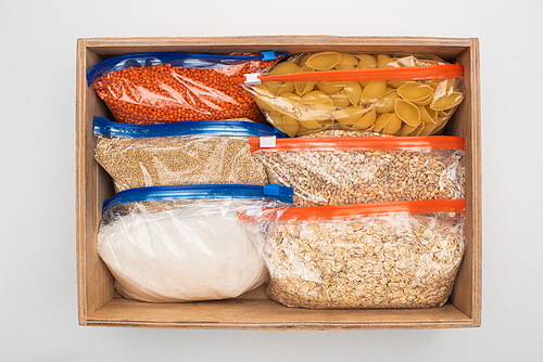 top view of pasta and groats in zipper bags in wooden box on white background, food donation concept