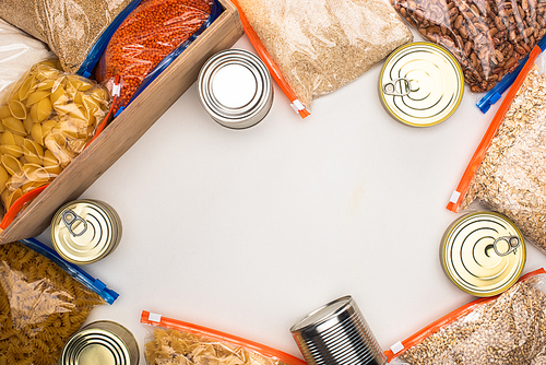 top view of cans and groats in zipper bags with wooden box on white background, food donation concept