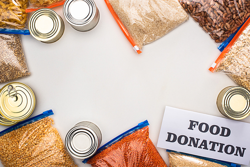 top view of cans and groats in zipper bags near card with food donation lettering on white background